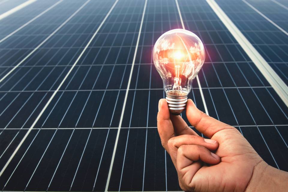 a man holding a bulb in front of residential solar panels